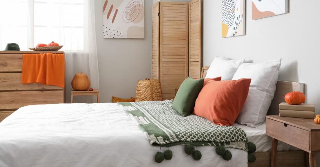 Dormitorio decorado en tonos otoñales con cojines verdes y caldera, manta tejida y detalles naturales.