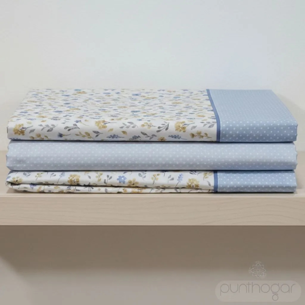 Sábanas MILOS color celeste de ABECÉ dobladas en estantería, diseño floral con detalles en azul y lunares blancos.